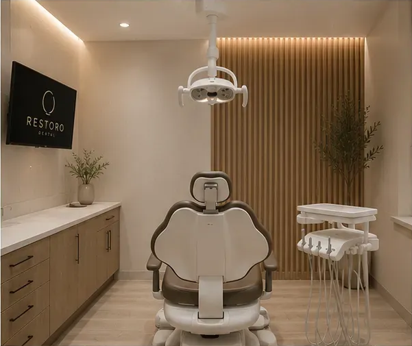 A Restoro operatory: dental chair, warm wood-slat wall, and the ring logo lit on a wall-mounted screen